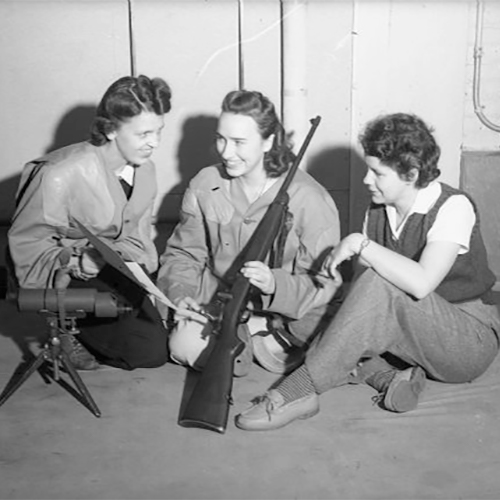 Three white women receiving weapons training during World War II. Women are receiving training on the handling of a rifle.